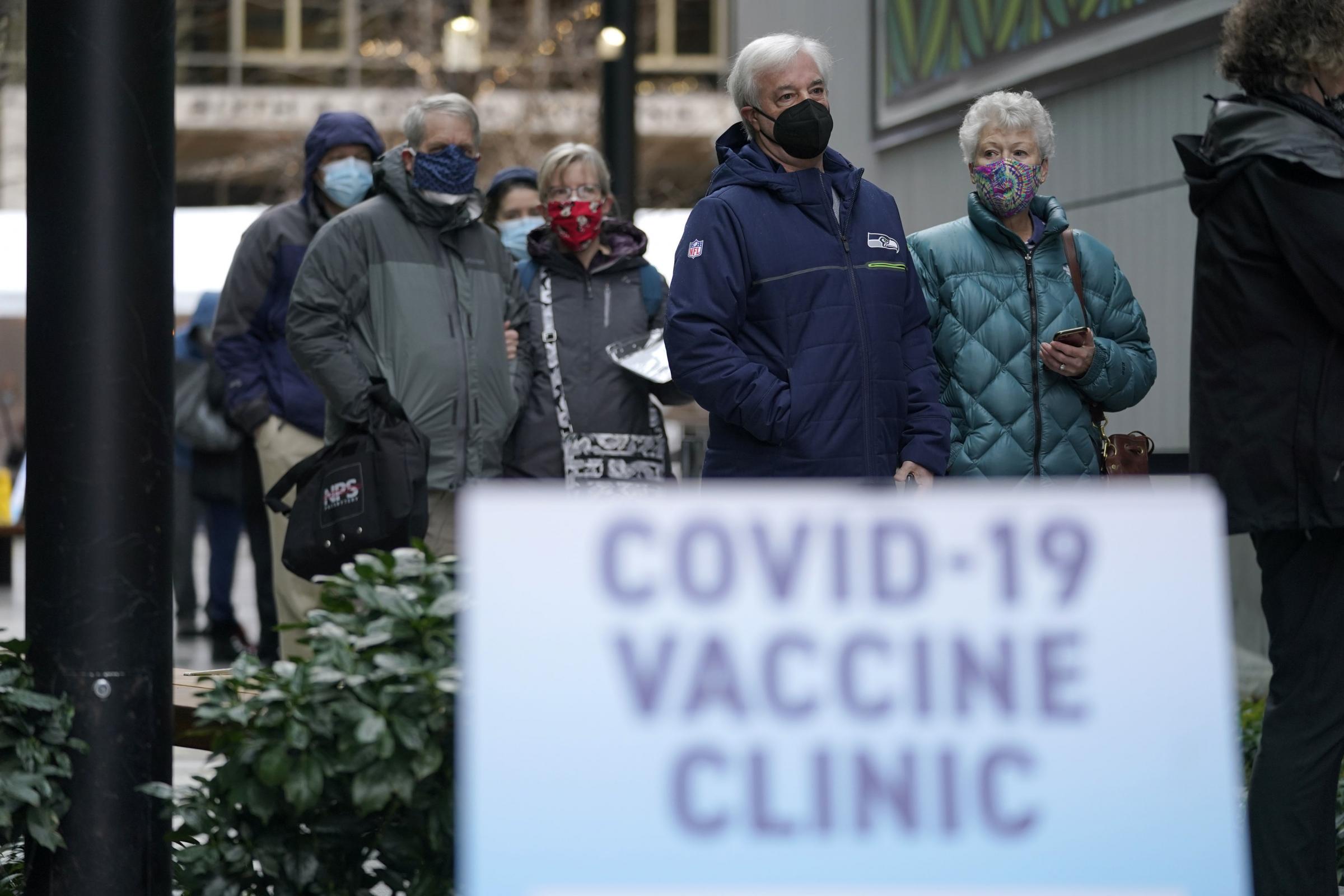 FILE - In this Jan. 24, 2021, file photo, people stand near a sign as they wait in line to receive the first of two doses of the Pfizer vaccine for COVID-19, at a one-day vaccination clinic set up in an Amazon.com facility in Seattle and operated by Virgi